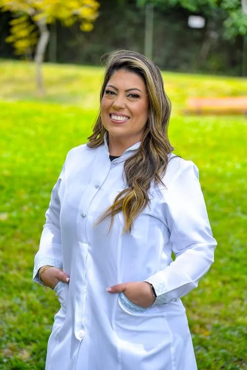 Kelly Guimarães de jaleco branco em uma área verde.